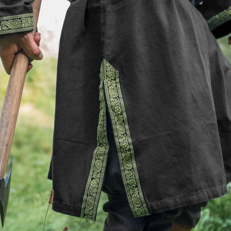 Black cotton Renaissance tunic with green embroidered trim on knee-length slits.