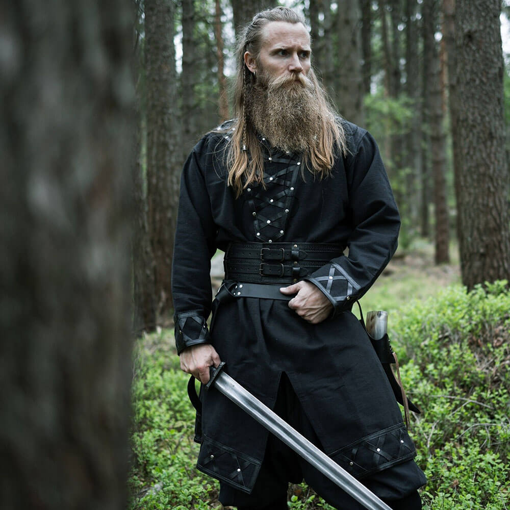 Man in black Renaissance tunic with leather accents, holding a sword in a forest.