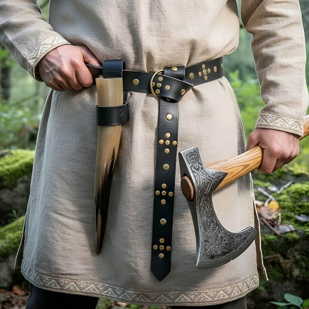 Riveted black leather Renaissance belt with ring loop and knotted design, worn over a beige tunic, holding a drinking horn and an engraved Viking axe.