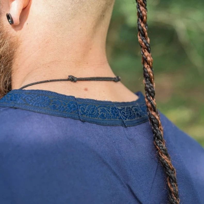 Blue cotton Renaissance tunic with intricate embroidered trim on the neckline, worn by a person with braided hair.