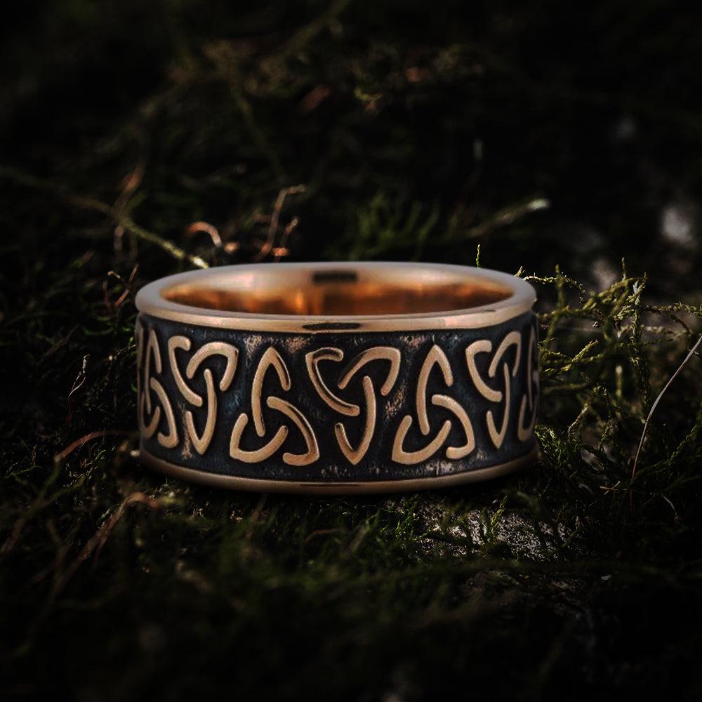 Bronze Renaissance Triquetra ring, handcrafted with a dark patina and polished edges, resting on moss.