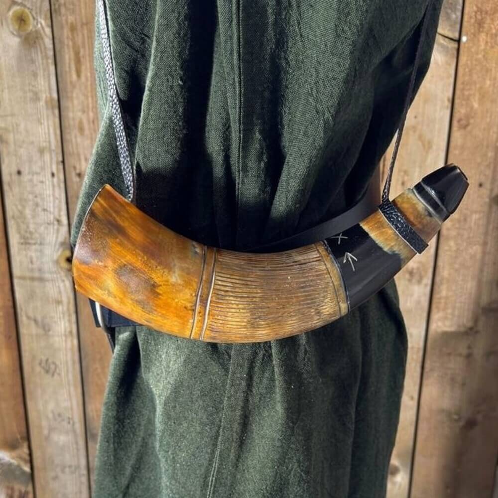 Renaissance blowing horn, polished natural horn with dark tip, metal mouthpiece, and leather strap on green tunic.