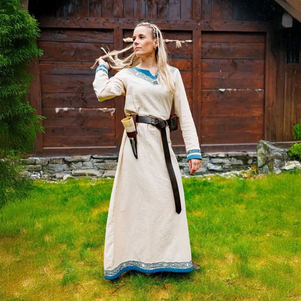 Ivory cotton Renaissance dress with blue trim, long sleeves, and A-line silhouette, worn by a woman outdoors.