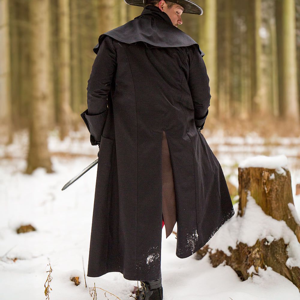 Renaissance black canvas pirate overcoat with shoulder mantle and rear split in snowy woods.