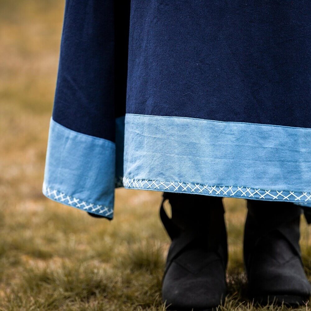 Dark blue Renaissance dress with light blue trim and white cross-stitch embroidery, worn over black boots.