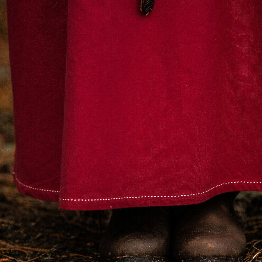 Rich red Renaissance cotton underdress with white decorative stitching along the hem, worn over dark boots.