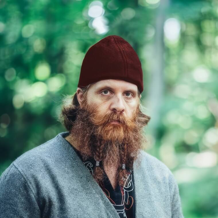 Man wearing a red wool Renaissance Ari cap with conical shaping and reinforced edges.
