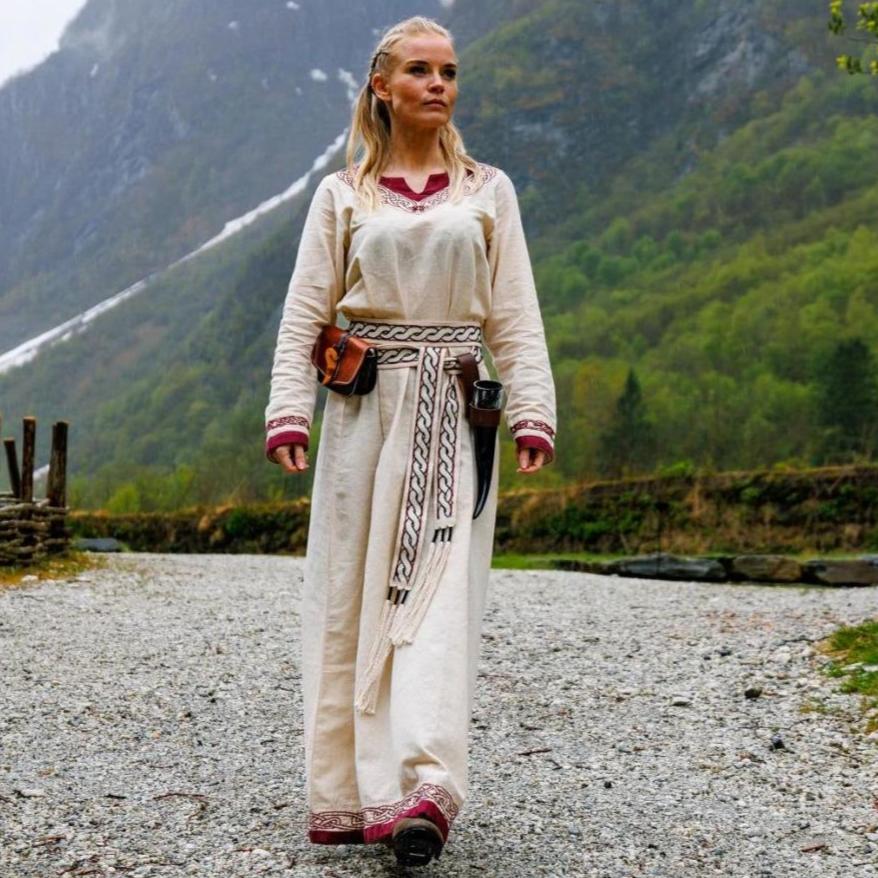 Renaissance ivory cotton dress with red trim, A-line silhouette, worn by a woman outdoors.