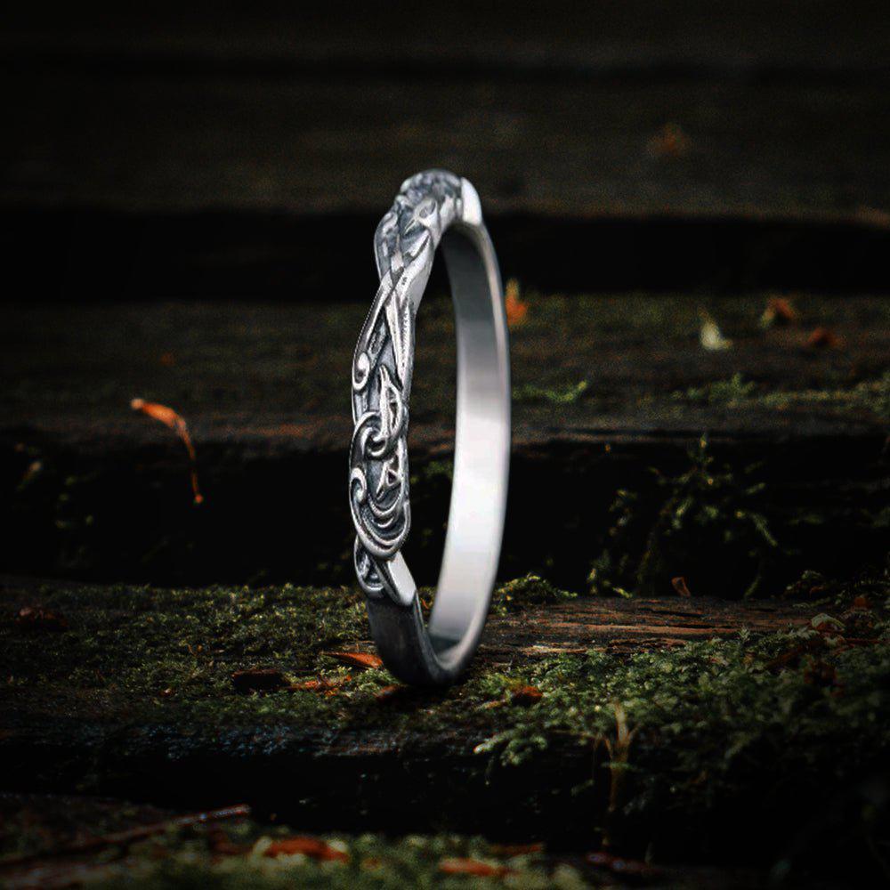 Sterling silver Renaissance raven ring with intricate scrollwork, shown on a mossy wooden surface.