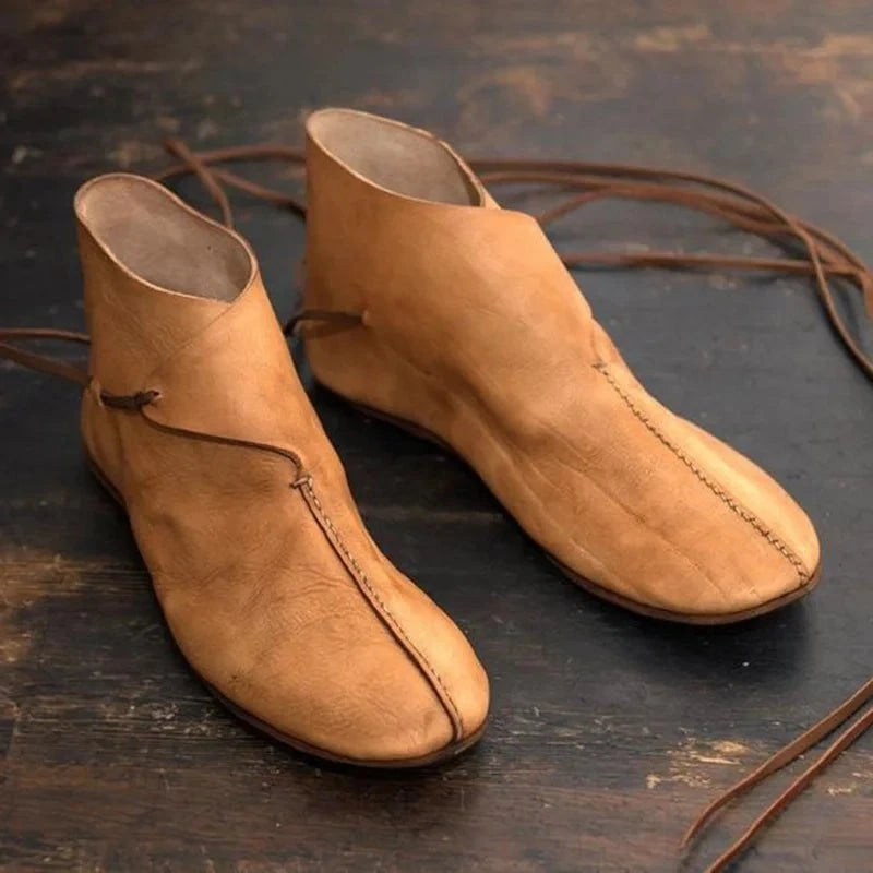 Pair of light brown PU leather Renaissance boots with laces on a dark wooden surface.