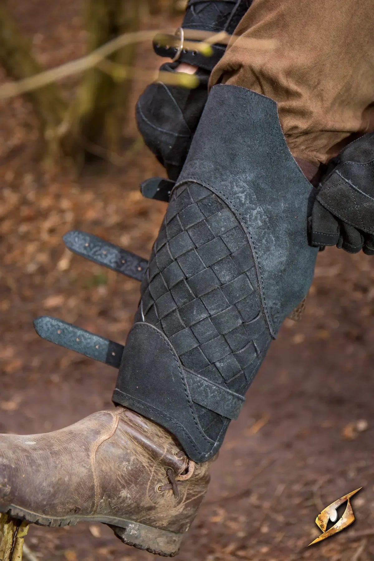 Renaissance black woven leather greaves with brass buckles, worn over a brown boot and pants.