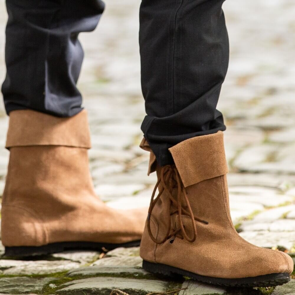 Person standing on cobblestones wearing Renaissance Sigurd brown suede boots with soft fold-over tops and side laces.