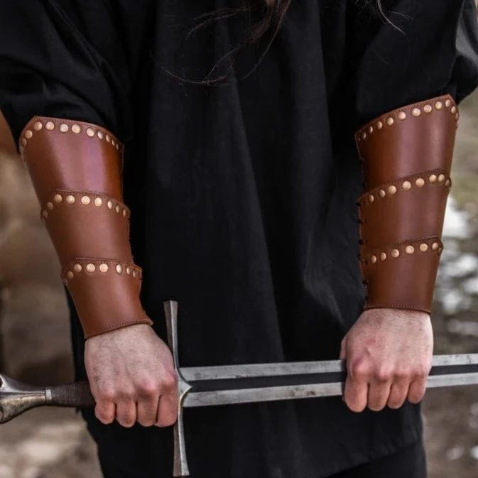 Brown leather Renaissance vambraces with rivet detailing, worn on forearms, holding a sword.