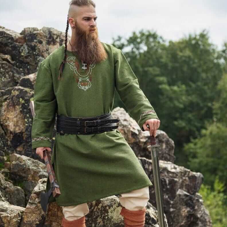 Man in a long-sleeve green Renaissance tunic with hand-embroidered neckline, leather belt, and sword.