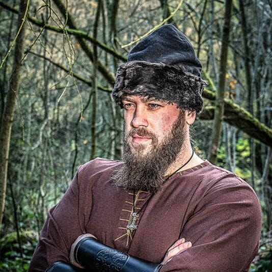 Renaissance fur-trimmed black cotton medieval cap on a bearded man in a forest.