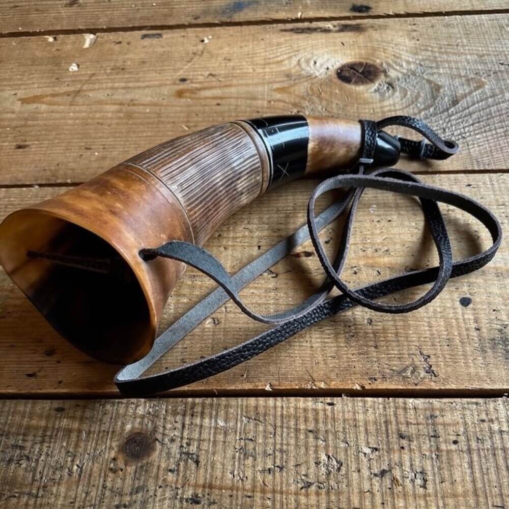 Renaissance blowing horn, polished natural horn with dark metal mouthpiece and black leather strap on wood.