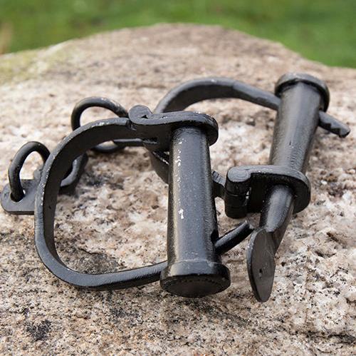 Darkened mild steel Renaissance manacles with adjustable crossbar lock and connecting chain on a rock.