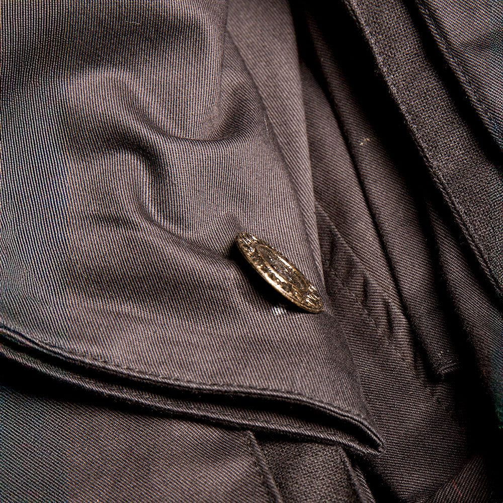 Close-up of a black canvas Renaissance pirate overcoat with an ornate metal button and textured fabric.
