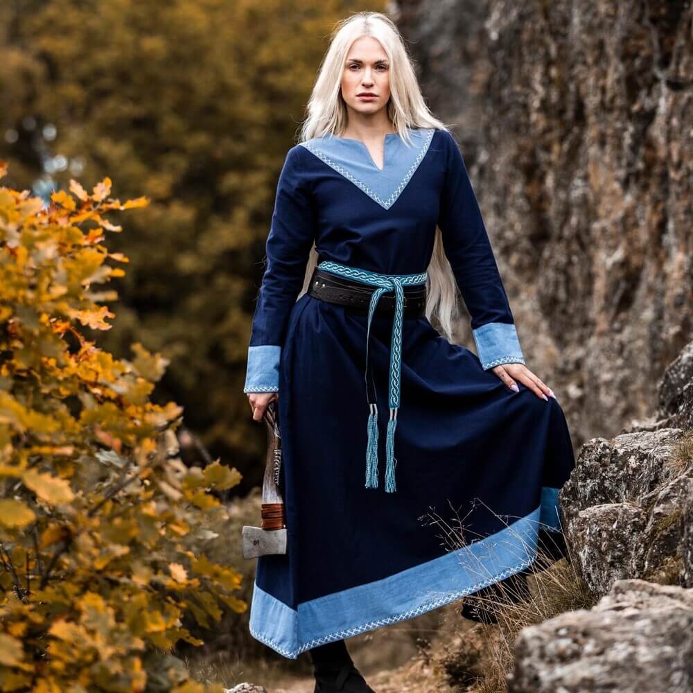Dark blue Renaissance dress with light blue trim, V-neck, and cross-stitch embroidery, worn by a woman outdoors.