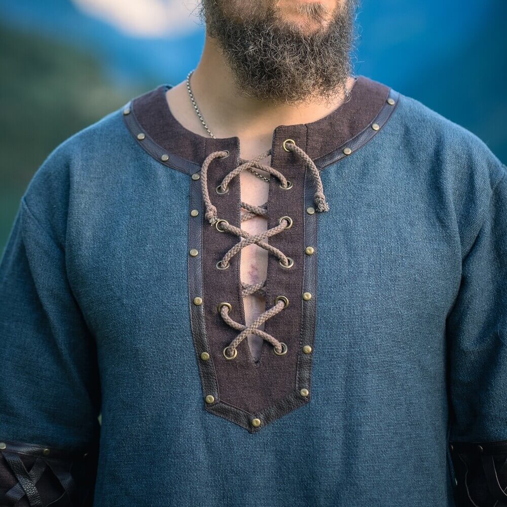 Blue Renaissance tunic with ornate leather trim, metal rivets, and crisscross lacing at the V-neck.