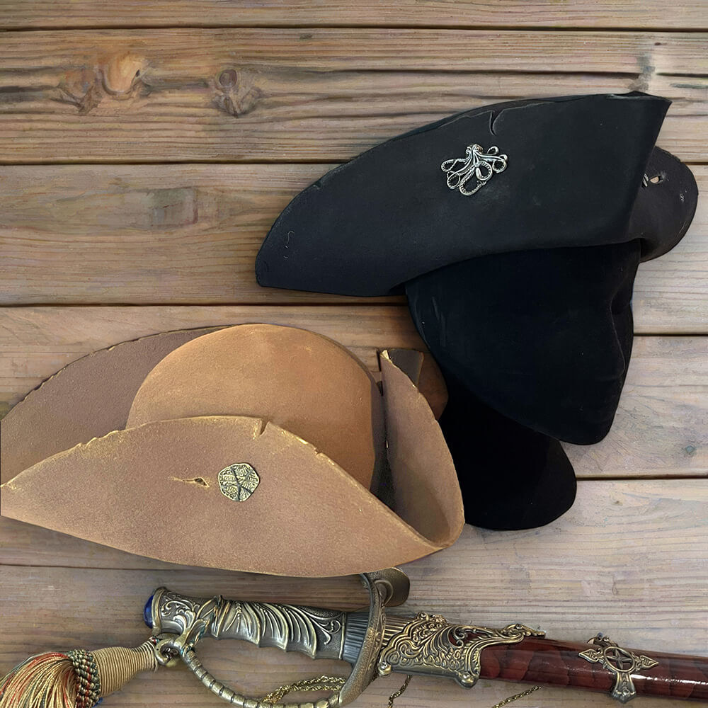 Weathered black and tan Renaissance pirate tricorn hats with a decorative sword on wood.