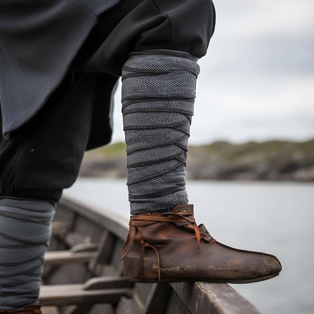 Person wearing grey Renaissance leg wraps and brown leather shoes with a blurred natural background.