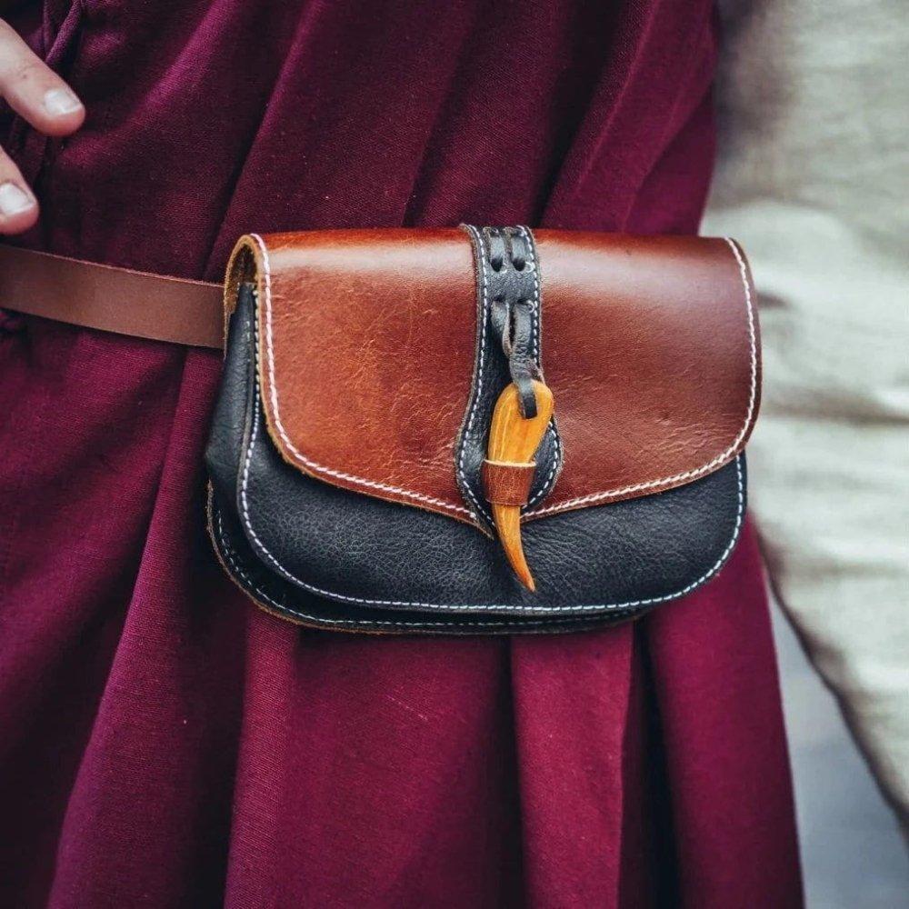 Renaissance artisan brown and black leather belt pouch with a wooden clasp on a burgundy tunic.