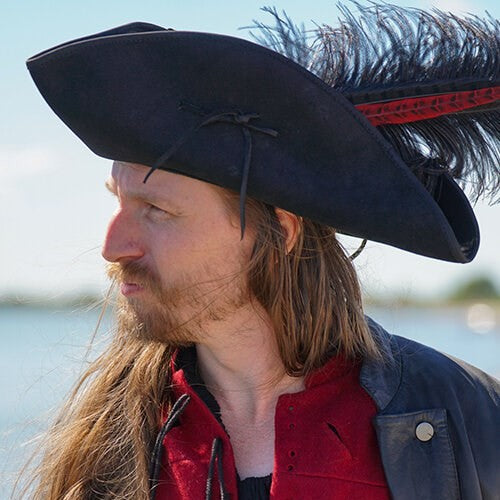 Black leather Renaissance tricorn hat with a feather plume, worn by a man with long hair.