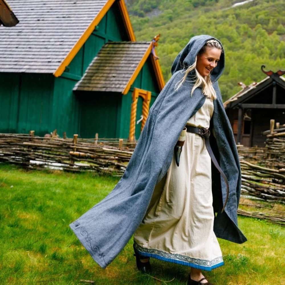 Woman in a gray Renaissance wool cloak with an extended hood and hand-stitched embroidery, walking outdoors.