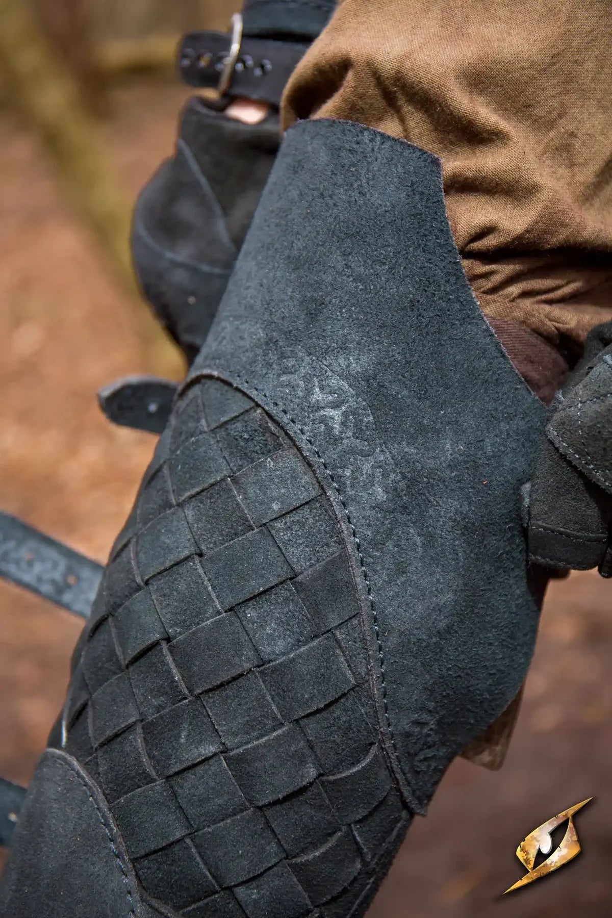 Black Renaissance woven leather greave with brass buckles, protecting a leg.