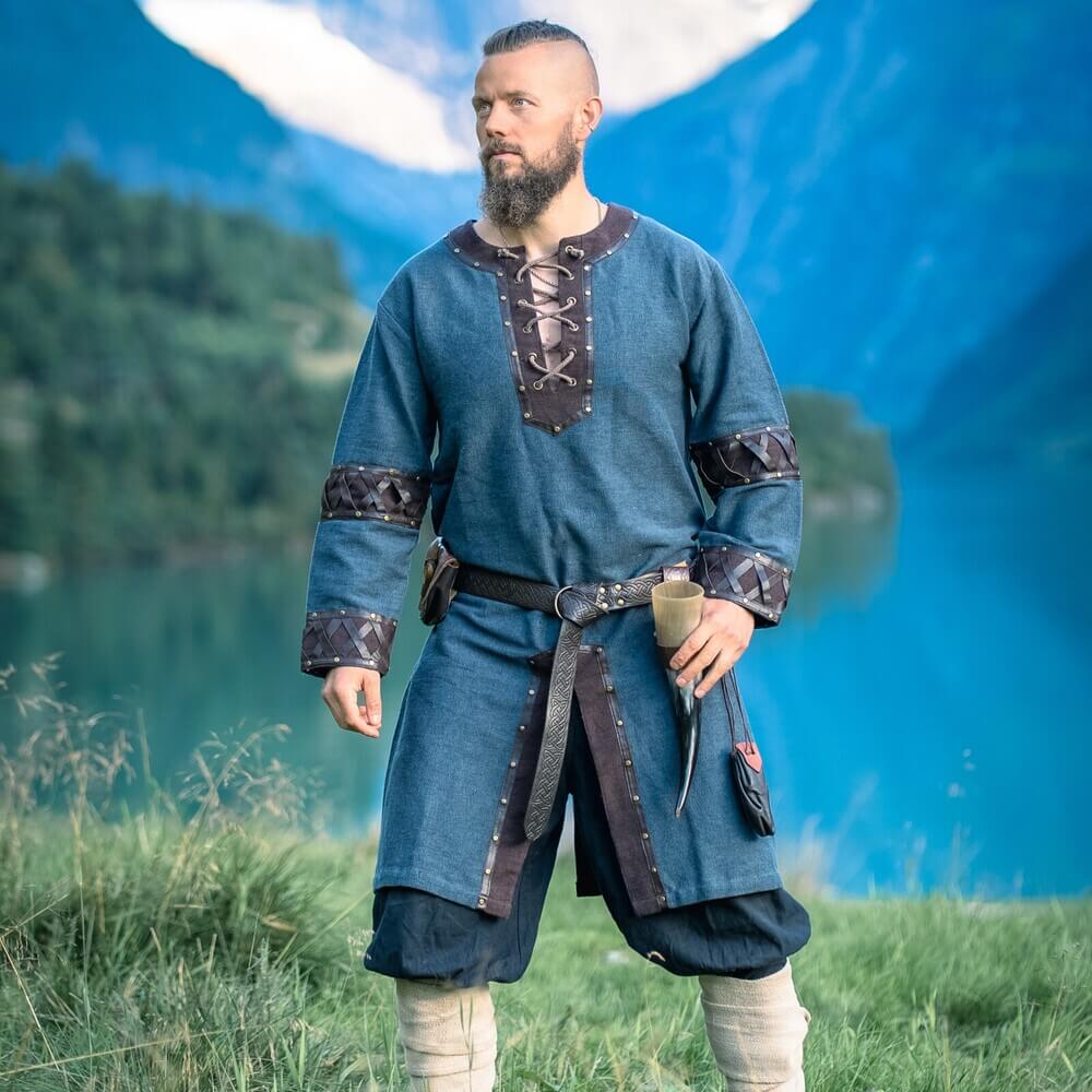 Man wearing Renaissance Tunic - Blue with Ornate Leather Trim, laced collar and leather cuffs, standing by mountain lake.