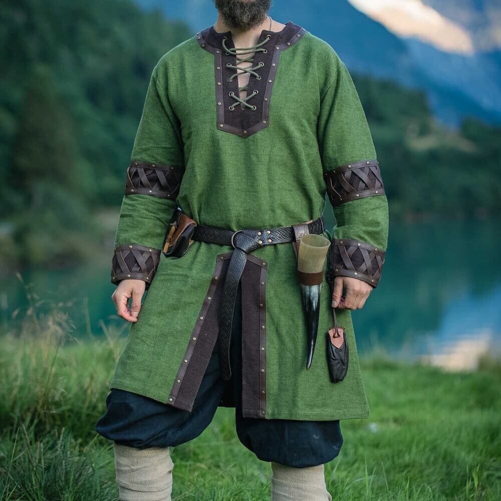 Man wearing Renaissance Tunic - Green with Ornate Leather Trim, laced neckline and leather cuffs, standing by mountain lake.